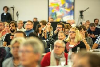 Menschen unterschiedlichen Alters und aus allen Bildungsschichten sitzen beim Bürgerinnenrat zusammen und lauschen den Vorträgen.